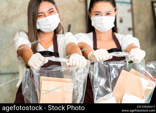 Close up waitress wear protective face mask smile and hold shopping bag for take away or takeout food. This essential service is very popular while city...
