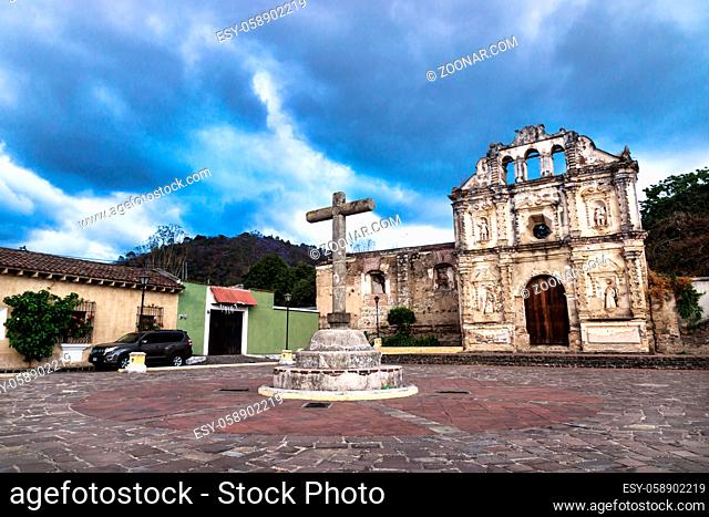 Antigua, Guatamala - 23 March 2018: Church fassade ruin of Ermita de Santa Isabel and cross on plazawith dramatic blue cloudscape