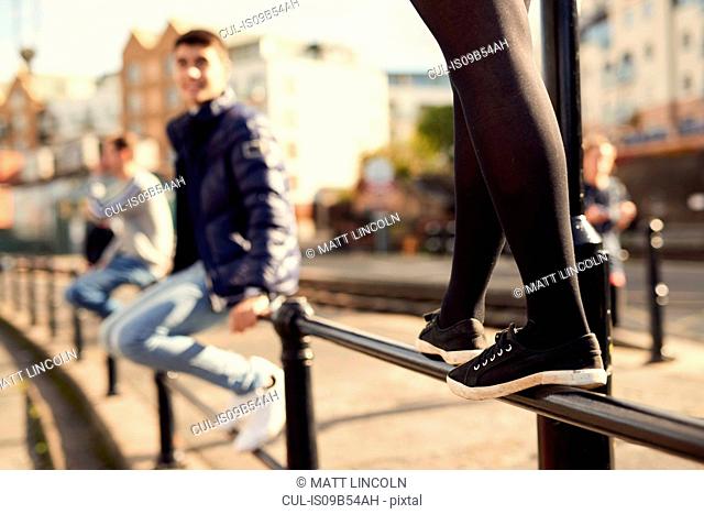 Young man sitting on railing, young girl walking along railing next to him, Bristol, UK