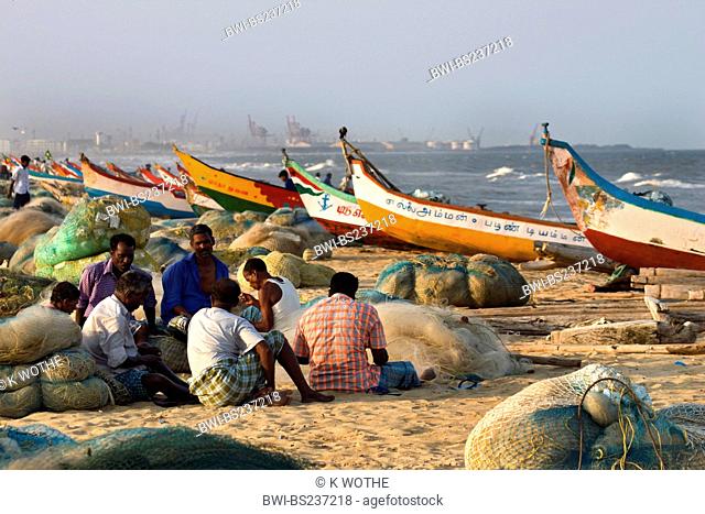 fishermen sitting on sand beach among their boats and nets, India, Tamil Nadu, Marina Beach, Chennai
