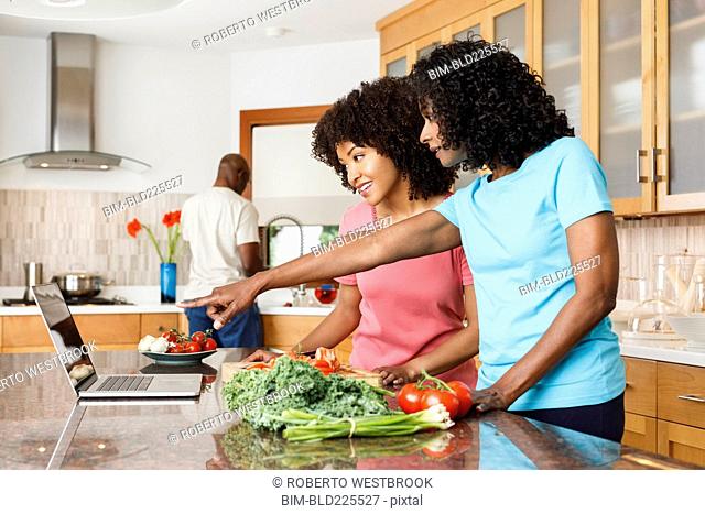 Black women using digital tablet and chopping vegetables in kitchen