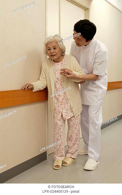 Male nurse helping senior woman walking in corridor