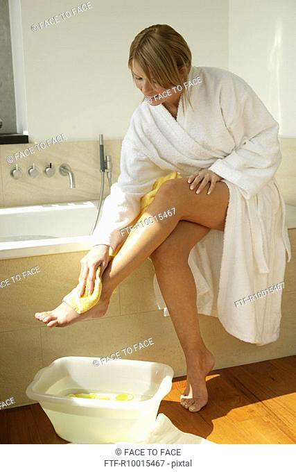 A woman wipes her leg as a small tub filled with yellow petals and water is kept beside her