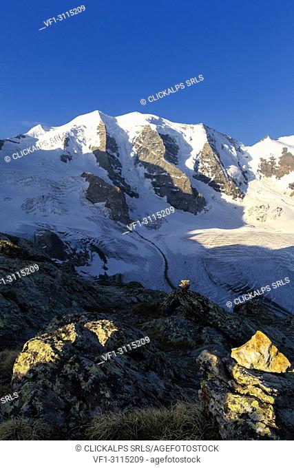 First sunlight illuminates rocks with Palù Peaks and Vedret Pers Glacier in the background. Diavolezza Refuge, Bernina Pass, Engadin, Graubünden, Switzerland