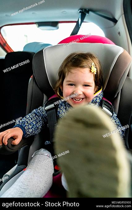 Portrait of laughing little girl sitting on child's seat in car