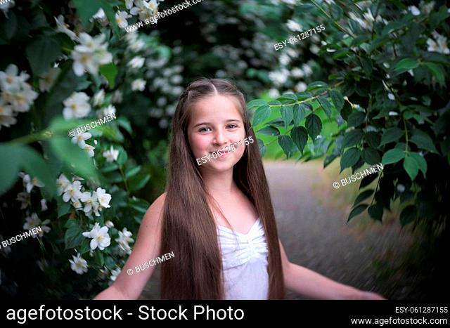 A beautiful girl with long hair stands in the flowering bushes of Philadelphus coronarius