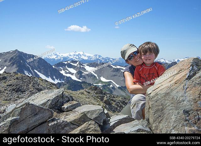 Woman and toddler son hikers pose for a photo from Grand View Peak (elev 6701') with Mount Olympus in the distance, Olympic National Park, Olympic Peninsula