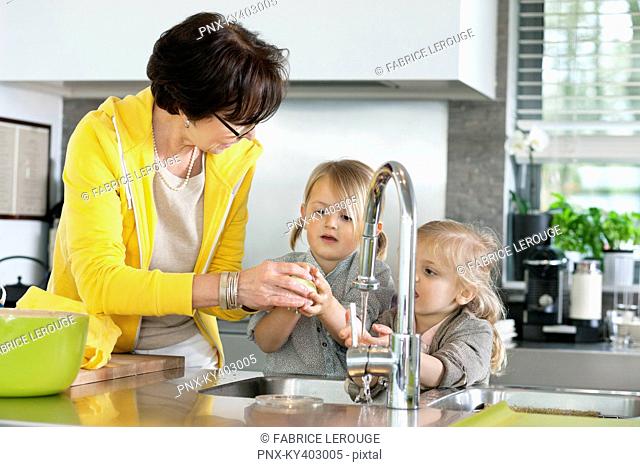 Elderly woman with her granddaughters washing in a kitchen