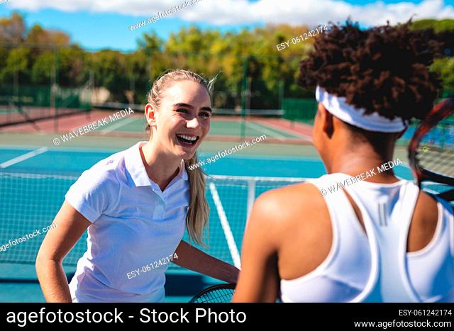 Cheerful caucasian female player looking at african american athlete at tennis court on sunny day