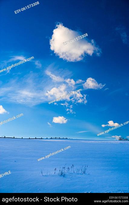 Post fence underneath clouds over a blue barren snowy winter landscape in the New England town of Stowe Vermont, USA