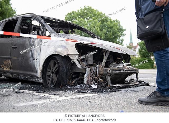 15 July 2019, Schleswig-Holstein, Lübeck: Jürgen Hinsch from Hanover stands next to his burnt-out VW car, which he parked in a car park near the old town island