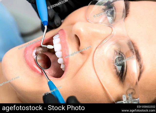 Charming girl in protective glasses. Her teeth are checking with the help of a dental bur and a dental mirror. Macro photo. Horizontal