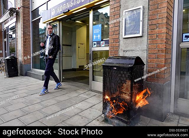 Stockholm, Sweden A pedestrian walks by a burning garbage can at the entrance to the Hornstull subway or Tunnelbana station