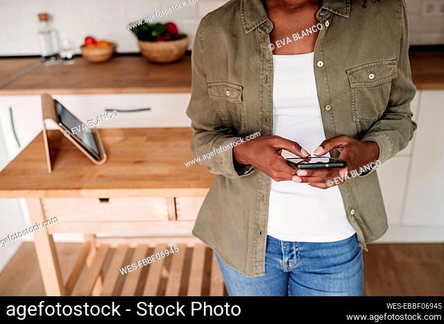 Woman using smart phone standing in kitchen at home