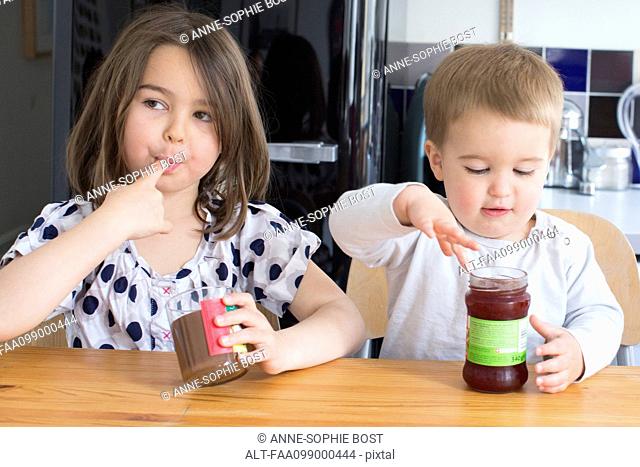 Young siblings tasting contents of jars with their fingers