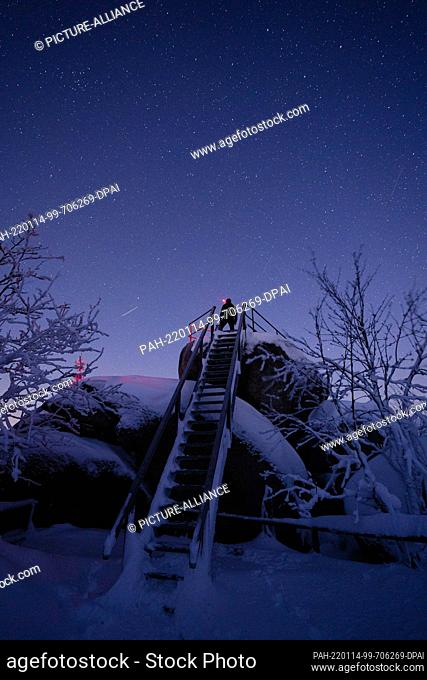 14 January 2022, Bavaria, Neubau: A man stands with a headlamp on the summit of the Nußhardt in the Fichtelgebirge under a clear starry sky