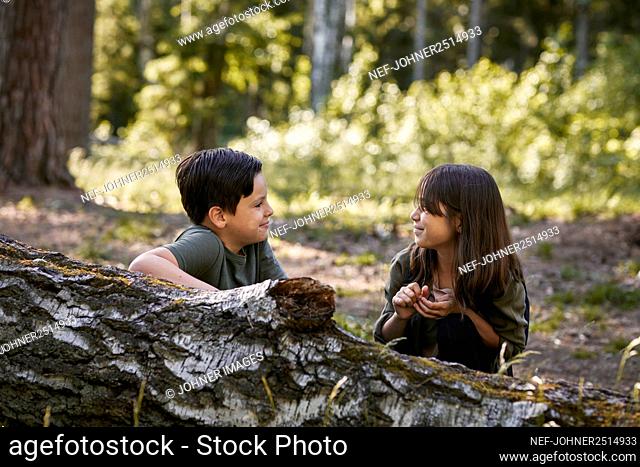 Boy and girl sitting near fallen tree in forest