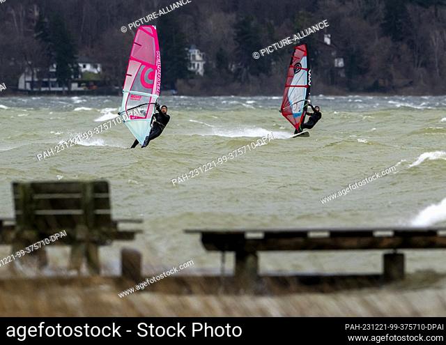 21 December 2023, Bavaria, Munich: Two surfers take advantage of the strong wind for their recreational sport on the Ammersee near Herrsching