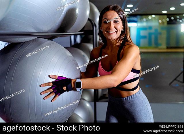 Smiling sportswoman holding fitness ball at gym