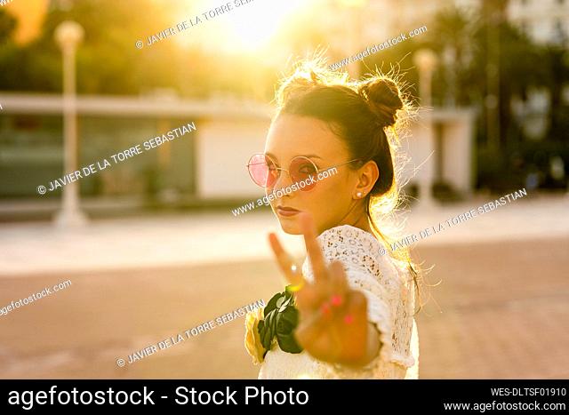 Teenage girl wearing red sunglasses showing peace sign in city
