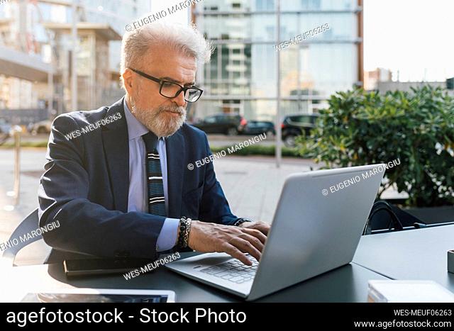 Senior businessman working on laptop sitting outdoors