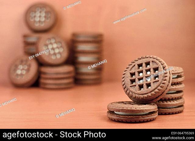 Chocolate sandwich round biscuits with vanilla cream filling on brown wooden table with copyspace. Still-life of sweet and tasty cookies with white cream...