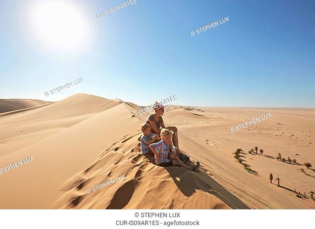 Mother and sons sitting on sand dune, Dune 7, Namib-Naukluft National Park, Africa