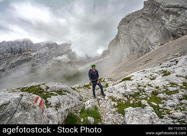 Hiker, climber on a trail between rocky cloudy mountains at Forcella Sore de la Cengia, Sorapiss circumnavigation, Dolomites, Belluno, Italy, Europe