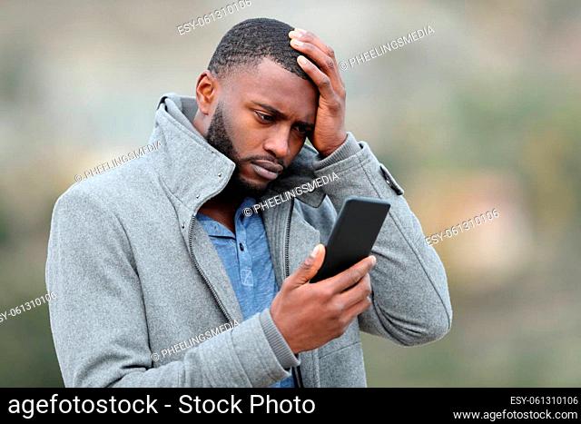 Worried man with black skin checking phone in winter