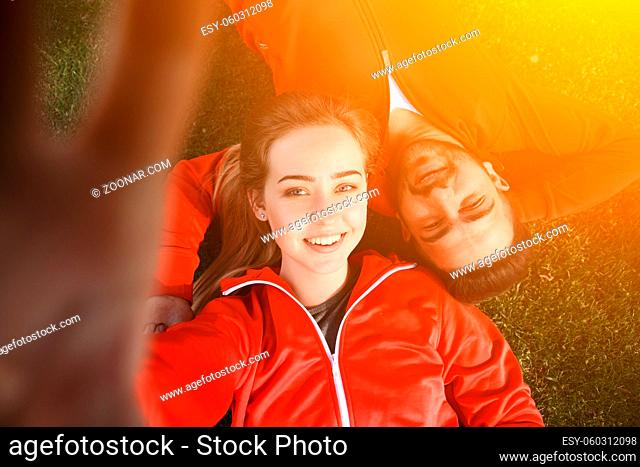 Happy sport man and woman making selfies in green park while lying on green grass after hard-working training: jogging, jumping, etc. Toned