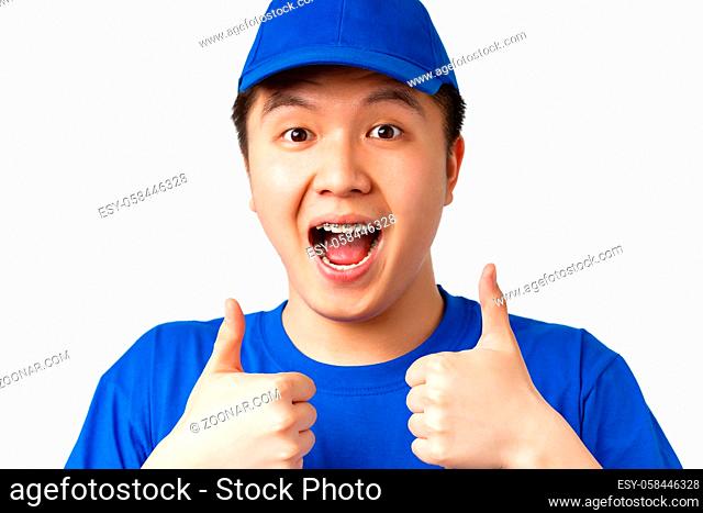 Online shopping, fast shipping, employees and home delivery concept. Close-up of excited happy asian male courier in blue uniform