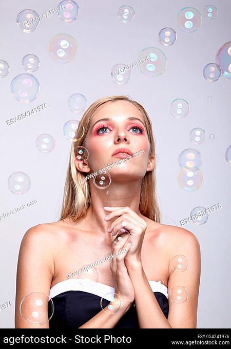Beautiful young blonde woman with soap bubbles. Female on grey background