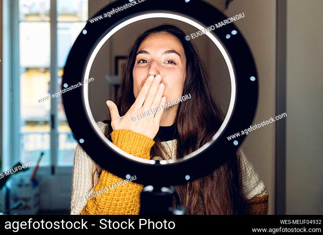 Influencer blowing kiss standing in front of illuminated ring light