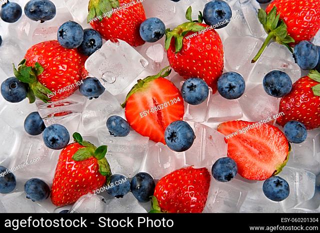Close up fresh red ripe strawberries, blueberries and ice cubes on table, elevated high angle view, directly above