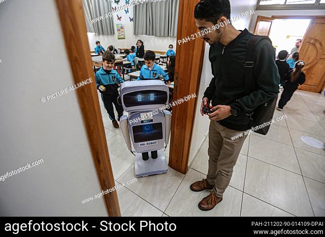02 December 2021, Palestinian Territories, Gaza City: Palestinian teacher Hassan Al-Razi controls a home-made talking educational robot after aiding him to...