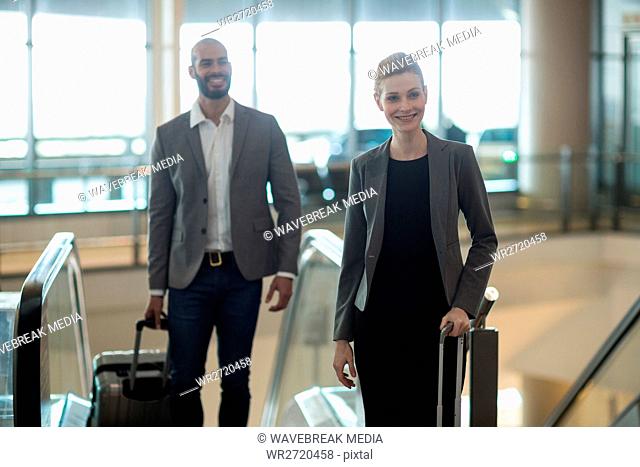Smiling businesspeople with luggage standing in front of an escalator