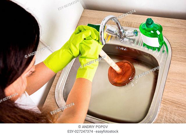 Close-up Of Person Using Plunger In The Kitchen Sink