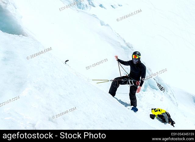 A professional mountaineer in a helmet and ski mask on the insurance does notch the ice ax in the glacier. The work of a professional climber in winter on a...