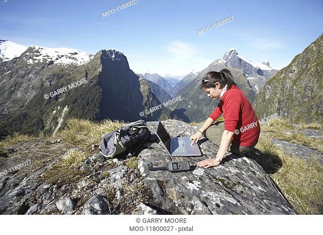 Woman using laptop on mountain peak