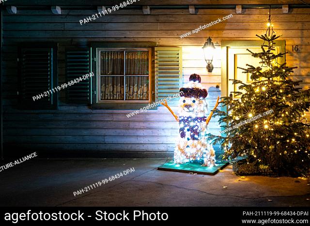 19 November 2021, Lower Saxony, Hanover: An illuminated snowman and a Christmas tree stand in front of a building at Hannover Adventure Zoo during the...