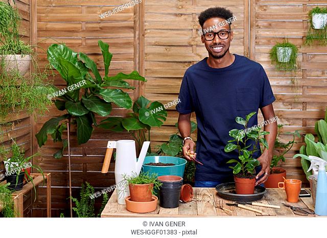 Portrait of a smiling young man repotting a plant on his terrace