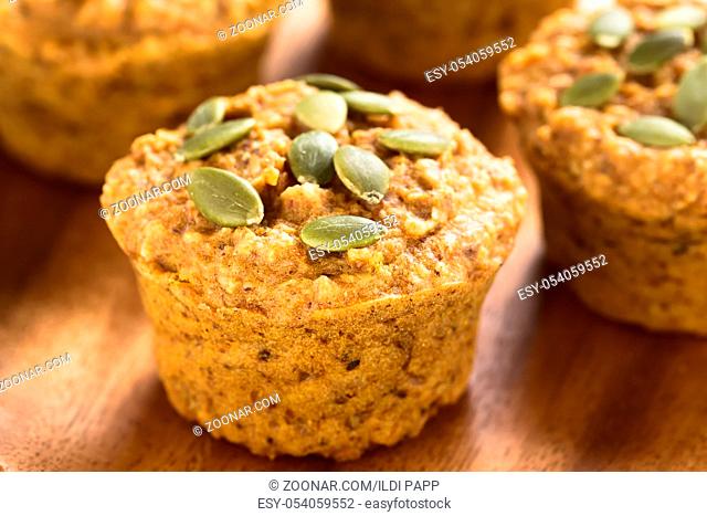 Fresh homemade pumpkin walnut oatmeal muffins with pepita pumpkin seeds on top on wooden plate (Selective Focus, Focus on the first seed on the muffin)