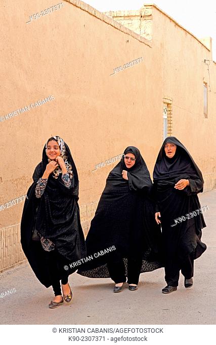 Three women walking along a street in the old town of Yazd, Iran, Asia