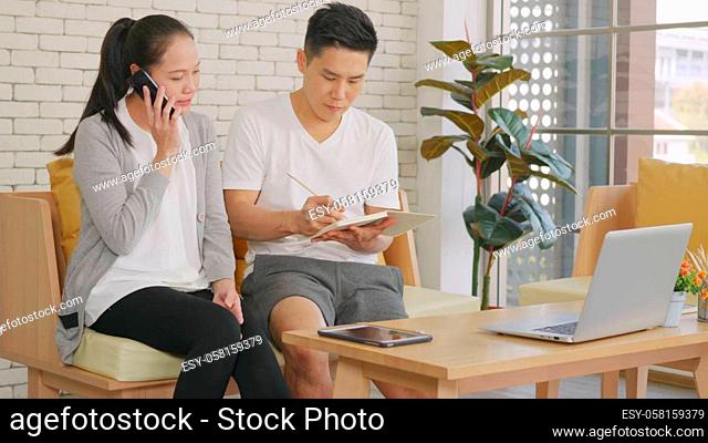 Happy Asian family couple husband and wife working confirming booking having talking call phone conversation and making writing notes of information together...