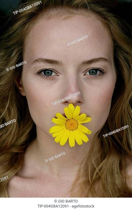 Portrait of woman with yellow flower in mouth