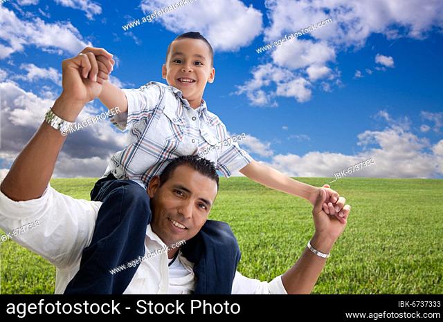 Happy hispanic father and son over grass field, clouds and blue sky