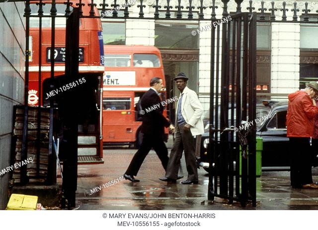 London Street Scenes -- a street with traffic and pedestrians seen through iron gates