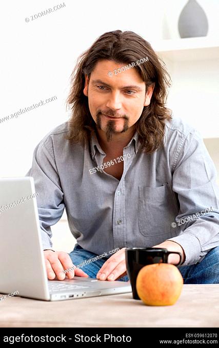 Casual man using laptop computer at home, smiling and looking at screen