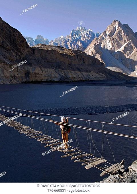 Trekker makes the crossing of the Hunza River in the Karakoram Mountains of Pakistan by rickety footbridge