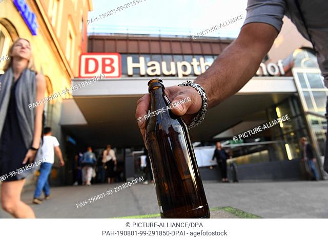 31 July 2019, Bavaria, Munich: A man holds a beer bottle in his hand in front of the north entrance of the HBF. The alcohol ban at Munich Central Station is now...
